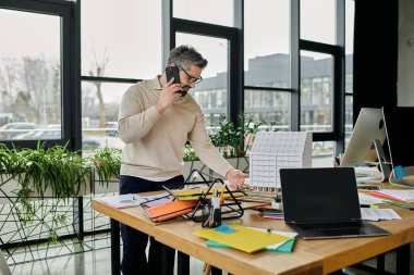 Sakallı yakışıklı bir işadamı modern bir ofiste çalışır. Telefonla konuşuyor ve masasının üstünde bir bina modeli var..