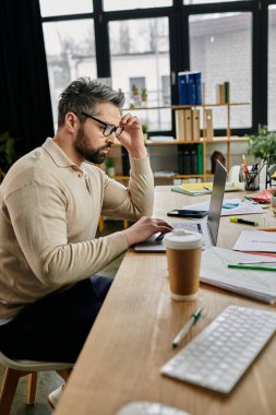 Sakallı yakışıklı bir işadamı modern ofis masasında dizüstü bilgisayarda çalışıyor..