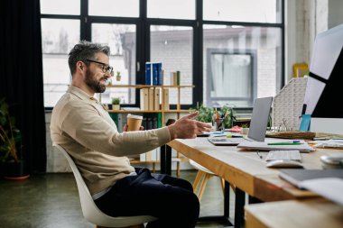 A handsome businessman with a beard sits at a desk in a modern office, engaged in a thoughtful conversation with someone off-camera. He holds a cup of coffee, his hand gesturing as he listens intently. clipart