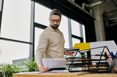 Sakallı yakışıklı bir işadamı modern ofis ortamındaki belgeleri inceliyor..