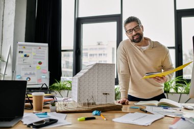 Sakallı yakışıklı bir işadamı modern bir ofisin planlarını ve model binasını inceliyor..