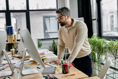 Sakallı yakışıklı bir işadamı modern ofis ortamında bilgisayarının başında özenle çalışıyor..