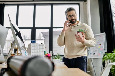 Sakallı yakışıklı bir işadamı modern bir ofiste duruyor. Renkli örnekleri inceleyip cep telefonuyla konuşuyor..