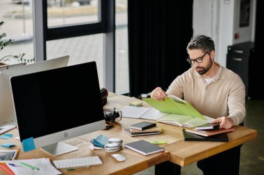 Yakışıklı, sakallı, gözlüklü bir işadamı modern bir ofiste masasında oturmuş belgeleri inceliyor..