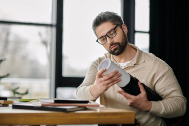Modern ofis ortamında yakışıklı, sakallı bir iş adamı yuvarlanmış bir tasarım projesini inceliyor..