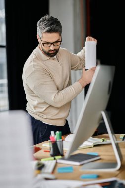 Sakallı yakışıklı bir işadamı modern bir ofiste bilgisayarla çalışıyor..