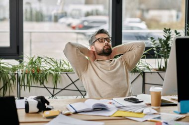 Sakallı bir işadamı, işine ara vermek için ofis koltuğuna yaslanıyor..