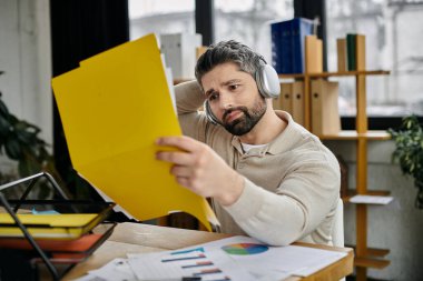 Sakallı yakışıklı bir işadamı kulaklık takıyor ve modern bir ofiste masasında dokümanları gözden geçiriyor..