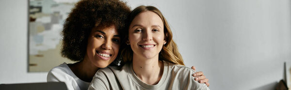 Two women, in casual attire, pose for a picture at home, smiling and embracing.
