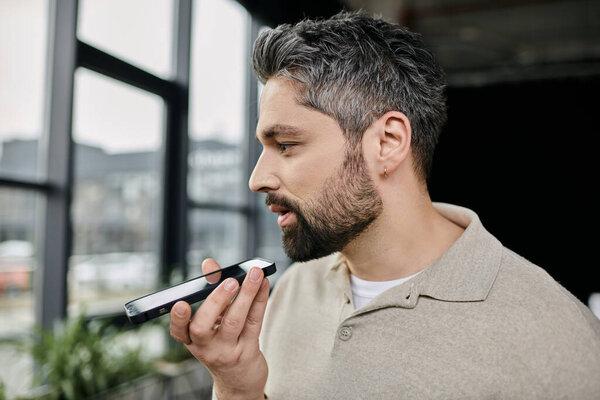 Красивый бизнесмен с бородой говорит в свой телефон, работая в современном офисе.