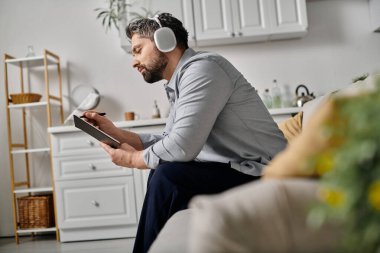 Kanepede elinde defterle günlük kıyafetlerle oturan sakallı bir adam..