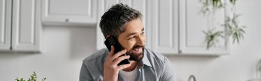Sıradan giyinmiş sakallı bir adam telefonuyla konuşurken gülümsüyor..