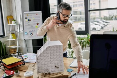 Modern ofisindeki bir binanın modelini incelerken gözlüklü yakışıklı bir iş adamı telefonuyla konuşuyor..