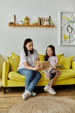 A mother and her daughter with a prosthetic leg are sitting on a yellow couch, reading a book together. clipart