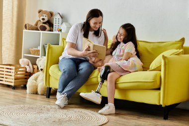 Esmer bir anne ve protez bacağı olan kızı sarı bir kanepede oturmuş birlikte kitap okuyorlar..