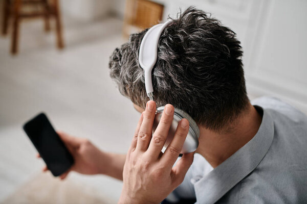 A man works from home while wearing headphones, holding a smartphone.