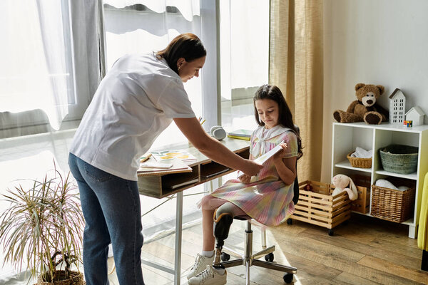 A brunette mother helps her daughter with a book at their home desk. The daughter has a prosthetic leg.