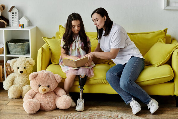 A brunette mother and her daughter, who has a prosthetic leg, are enjoying quality time together at home, reading a book on a yellow sofa.