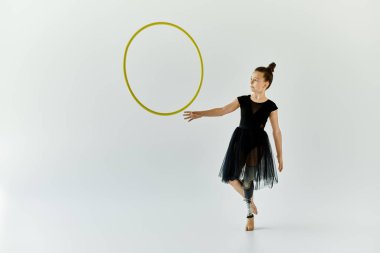 A young girl with a prosthetic leg practices gymnastics with a hoop in a studio setting. clipart