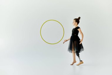 A young girl with a prosthetic leg practices gymnastics with a hoop in a studio. clipart
