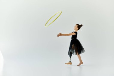 A young girl with a prosthetic leg practices gymnastics with a hula hoop in a white studio. clipart