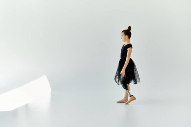 Siyah mayo ve etekli genç bir kız, beyaz bir stüdyoda protez bir bacak giyerken gücünü ve zarafetini sergiliyor..