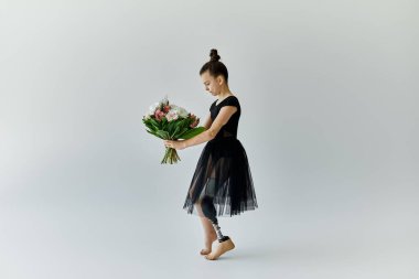 Protez bacaklı genç bir kız siyah jimnastik mayosu ve etek giyerken elinde bir buket çiçek tutuyor..