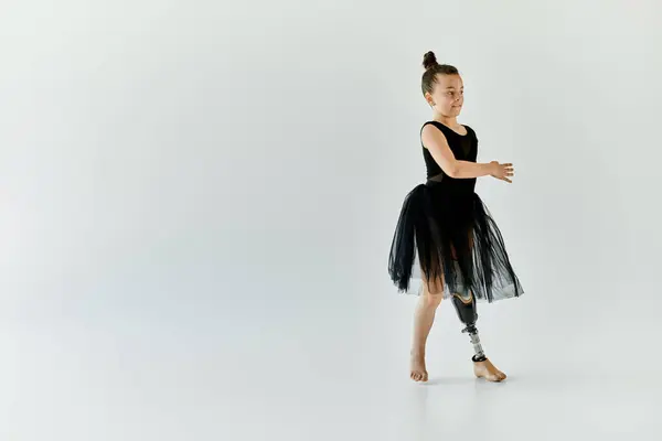 stock image A young girl with a prosthetic leg performs a graceful dance move in a black leotard and tutu.