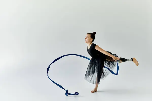 stock image A young girl with a prosthetic leg performs a graceful gymnastics routine with a blue ribbon.