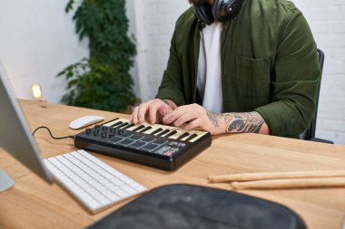 Kulaklık takan genç Asyalı bir adam stüdyosundaki bir masada oturup müzik bestelerken MIDI klavyesi çalıyor..