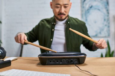 Asyalı bir adam stüdyosunda elektronik davul çalıyor..