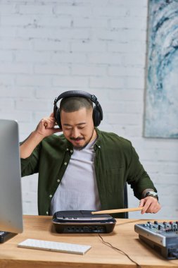 Asyalı bir adam müzik stüdyosunda bateri çalar, kulaklıkları takar ve sanatına odaklanır..