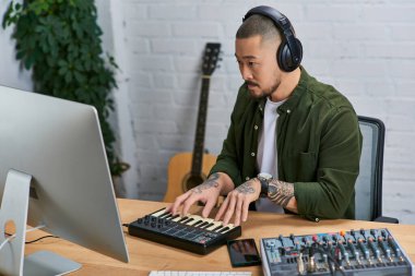 Asyalı bir adam stüdyosunda müzik aletleriyle çevrili bir Midi klavyesi çalıyor..