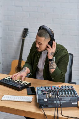 Asyalı bir adam stüdyosunda bir klavye çalar. Arka planda bir karışık tahta ve gitar vardır..