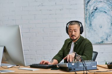 Kulaklık takan ve yeşil gömlekli yakışıklı bir Asyalı stüdyoda bir masada oturmuş müzik prodüksiyonu üzerinde çalışıyor..