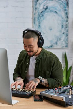 A young Asian man, wearing headphones, plays a keyboard in his studio. clipart