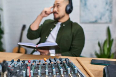 Günlük giysiler içinde Asyalı bir adam stüdyosunda oturmuş, müzik üzerinde çalışıyor..