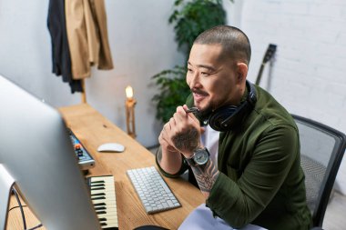 Yakışıklı bir Asyalı, çok enstrümanlı bir adam stüdyo masasında oturmuş, müzik üzerinde çalışıyor..