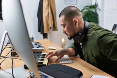 A handsome Asian man, a multi-instrumentalist, is seen in his studio playing a keyboard. clipart