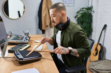 Yetenekli bir Asyalı stüdyosunda oturuyor, bagetleri kullanarak elektronik bir bateri platformunda müzik yapıyor..