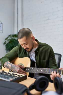 Yakışıklı bir Asyalı, çok enstrümanlı bir adam, stüdyosunda akustik gitar çalıyor..