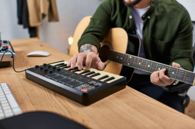 Stüdyosunda klavye ve akustik gitar çalan Asyalı bir adam..