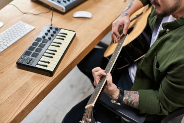 Yakışıklı bir Asyalı atölyesinde akustik gitar çalıyor. Etrafı müzik ekipmanlarıyla çevrili..