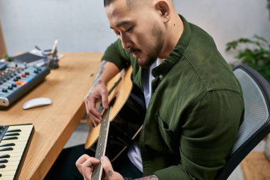 Genç Asyalı bir adam stüdyosunda akustik gitar çalıyor..