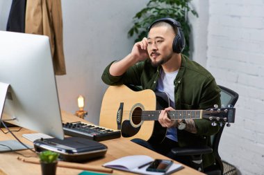 Yakışıklı bir Asyalı, sıradan giyinmiş, gitar çalıyor ve stüdyoda çalışırken müzik dinliyor..
