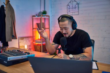 Yakışıklı bir Asyalı stüdyosunda bir podcast kaydediyor, kulaklık takıyor ve mikrofona konuşuyor..