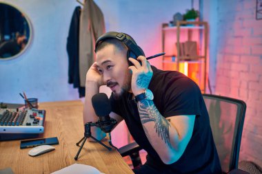 Yakışıklı bir Asyalı stüdyosunda kulaklık ve siyah tişört giyen bir podcast kaydediyor..