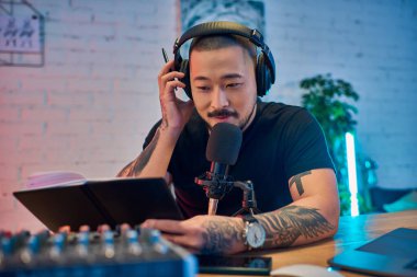 Kulaklık takan ve mikrofon takan Asyalı bir adam stüdyosunda bir podcast kaydediyor..
