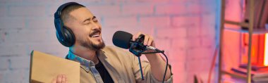 Yakışıklı bir Asyalı stüdyoda podcast kaydederken mikrofona gülüyor..