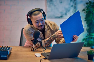 Kulaklık takan Asyalı bir adam stüdyosunda bir podcast kaydediyor..